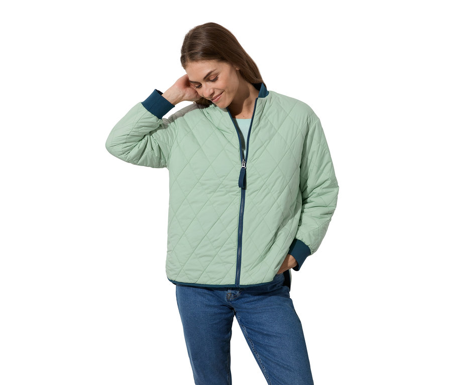 Frau trägt eine hellgrüne Wende-Steppjacke mit blauen Bündchen und Jeans.