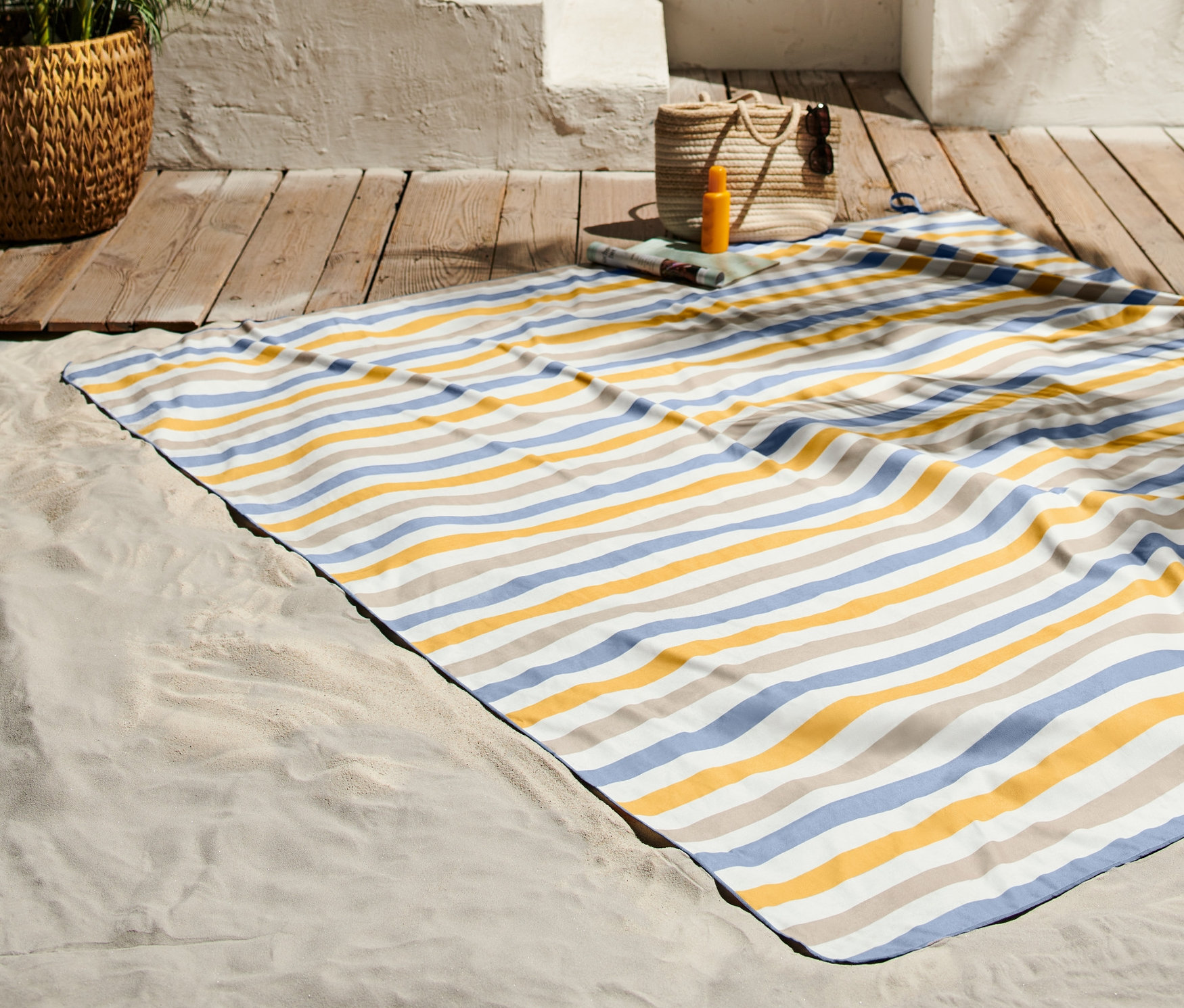 Ein extragroßes Strandtuch (ca. 2 x 2 m) liegt auf Sand neben einem Holzboden.