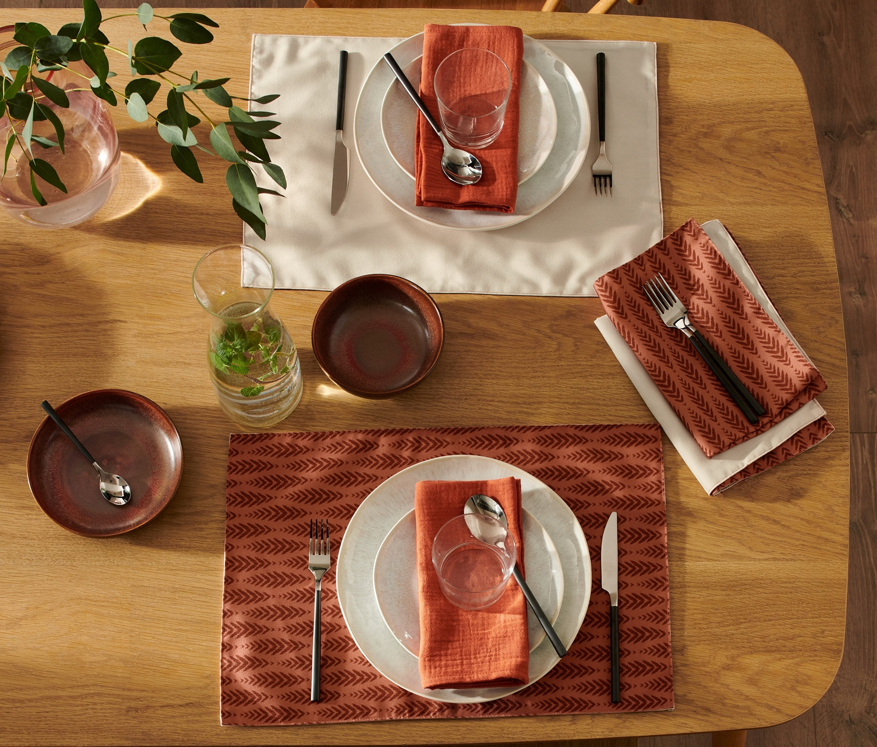 Zwei gedeckte Tische mit je 4 Wende-Platzsets, Tellern, Gläsern, Besteck und Servietten. Auf dem Tisch steht eine Vase mit Pflanzen.