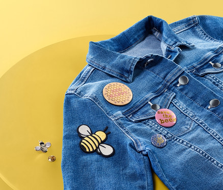 Eine Jeansjacke liegt auf einem gelben Tisch und trägt ein Anstecker-und-Bügelbild-Set »Biene«.