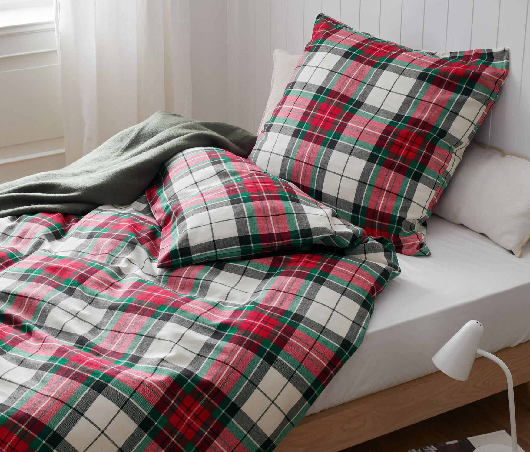 Auf einem Bett liegt Flanell-Bettwäsche mit einem rot, grün und weiß karierten Muster. Die Bettwäsche ist in Normalgröße, Übergröße und Doppelgröße erhältlich.