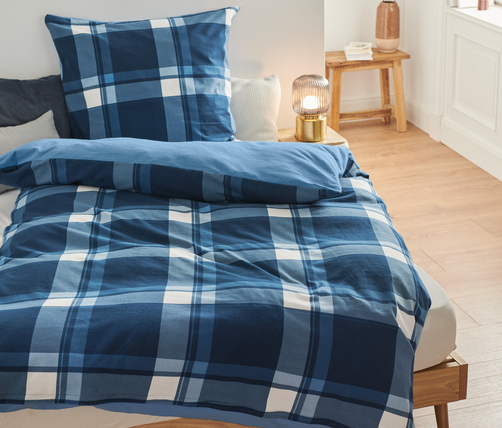 Auf einem Bett liegt Biber-Bettwäsche mit blauem Karomuster.