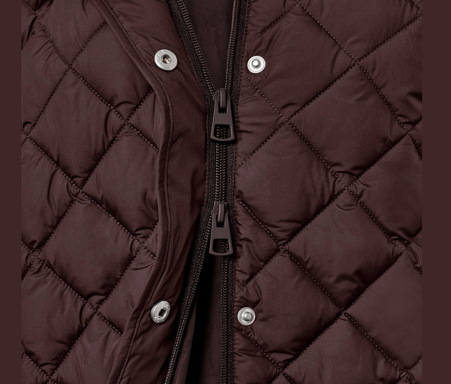 Detailaufnahme einer langen Steppweste mit Kapuze, die mit Reißverschluss und Druckknöpfen geschlossen wird.