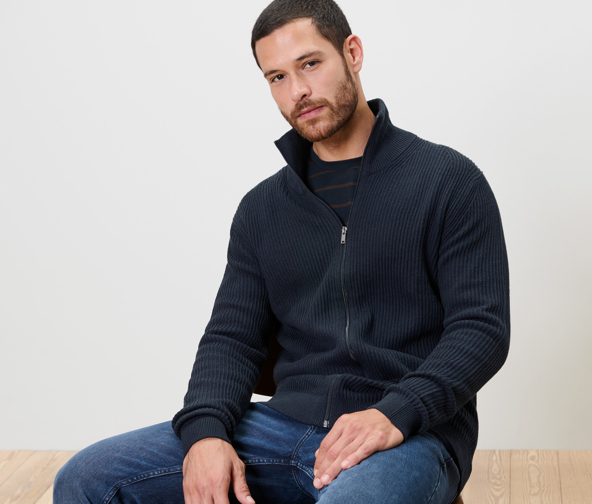 Mann sitzt auf einem Stuhl und trägt eine Strickjacke, navy.