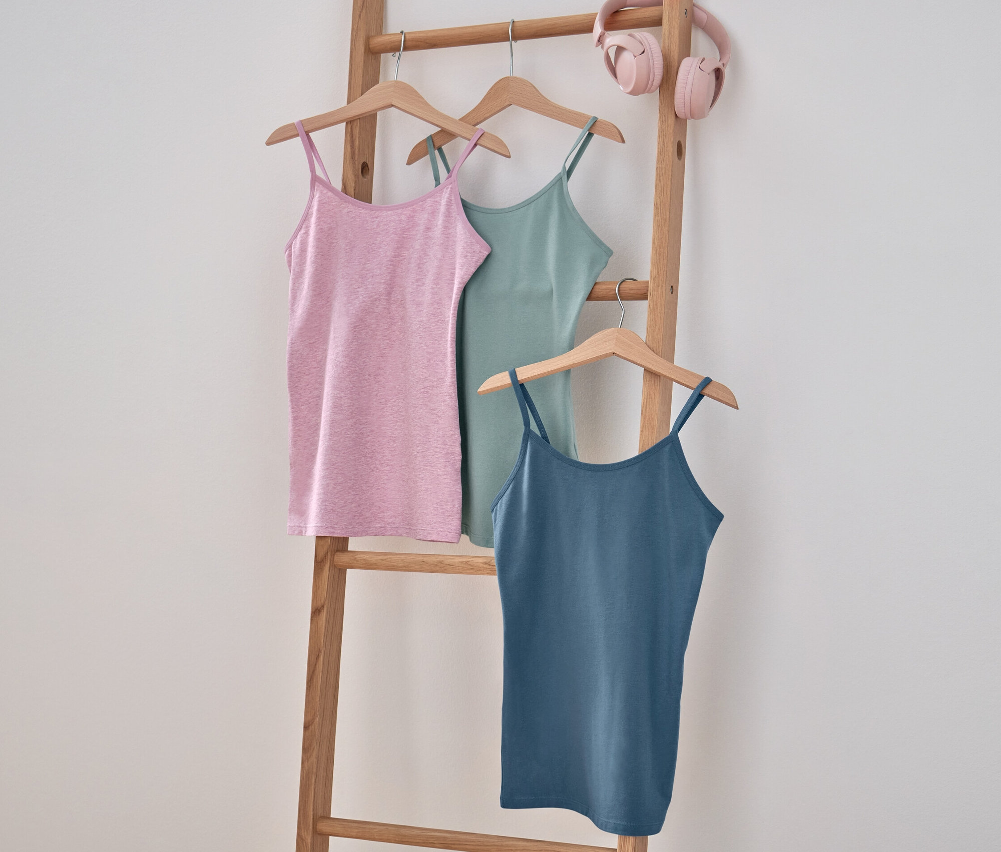 Drei Mädchen-Unterhemden hängen auf einer Holzleiter.