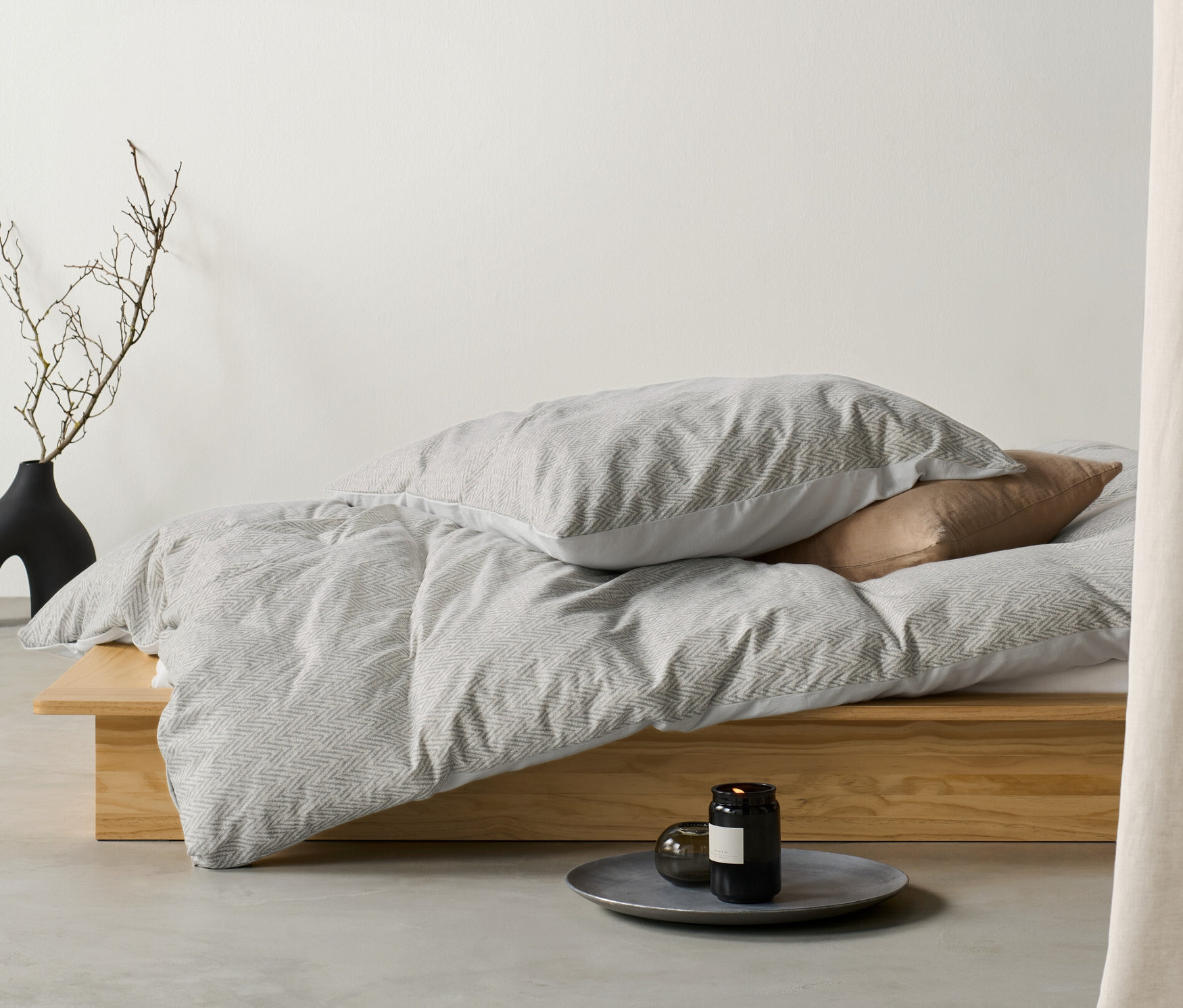 Winterjersey-Bettwäsche Normalgröße liegt auf einem Bett neben einer Vase mit Ästen.