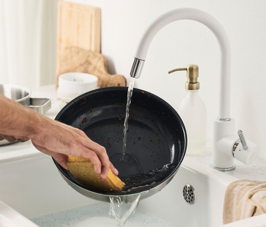 Mann spült eine ZWILLING Edelstahl-Bratpfanne, ca. 28 cm, mit einem Schwamm in einem weißen Spülbecken.
