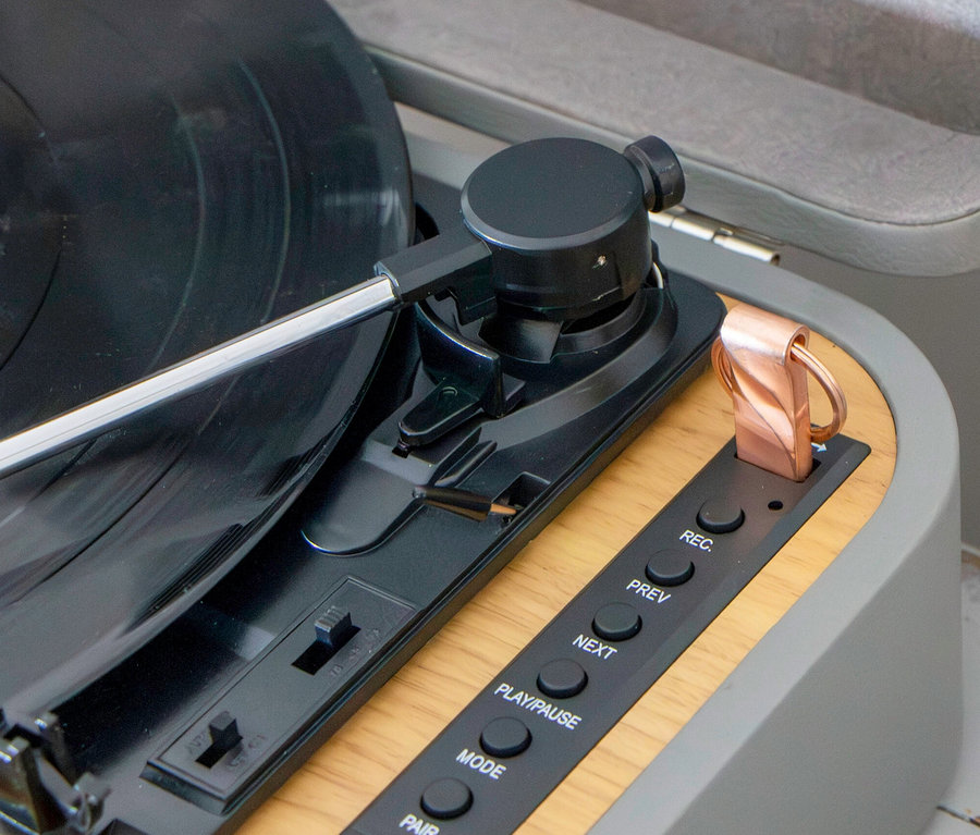 Detailaufnahme eines grauen Lenco Plattenspielers »TT-116« mit schwarzer Schallplatte, Bedienelementen und einem Kupferclip.