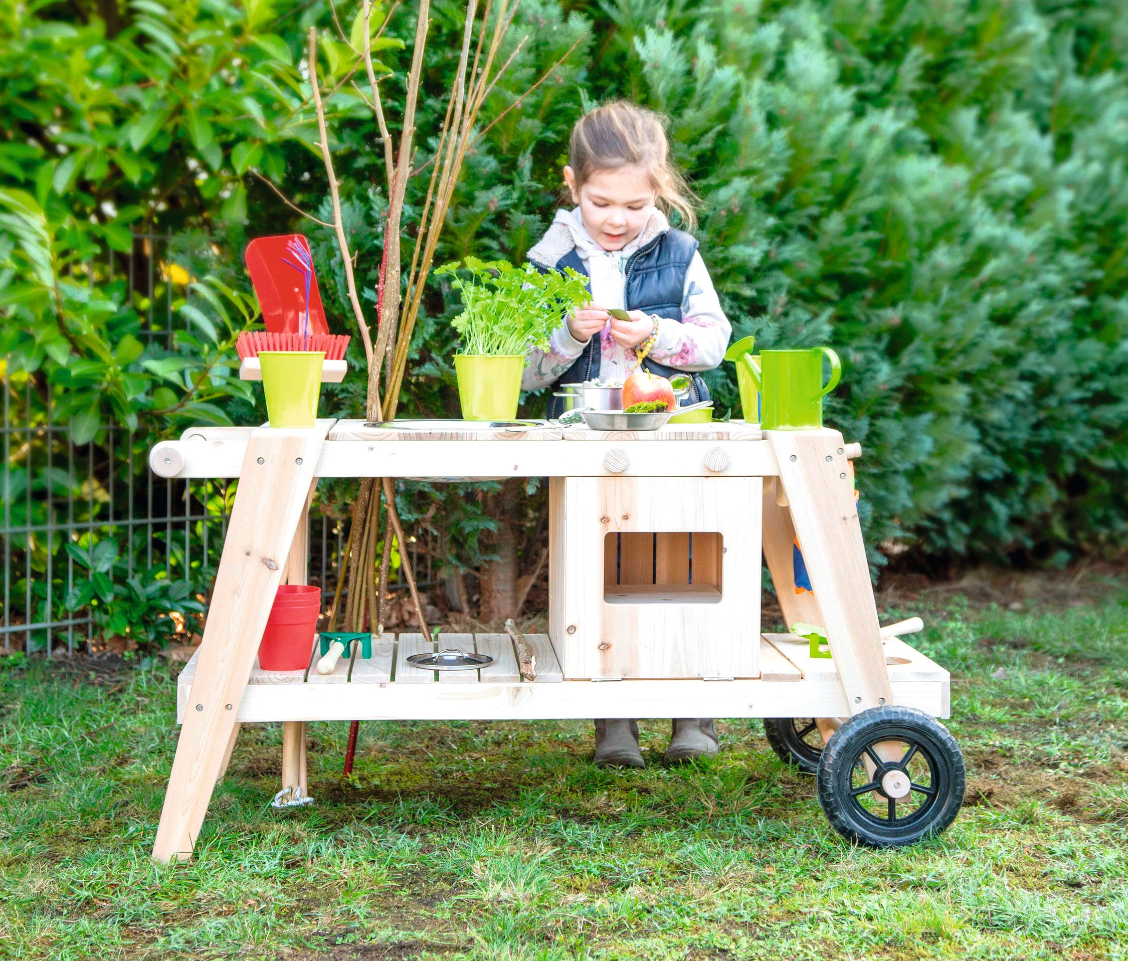 Mädchen spielt mit small foot Matschküche. Auf dem Tisch stehen Töpfe, Gemüse und Zubehör.