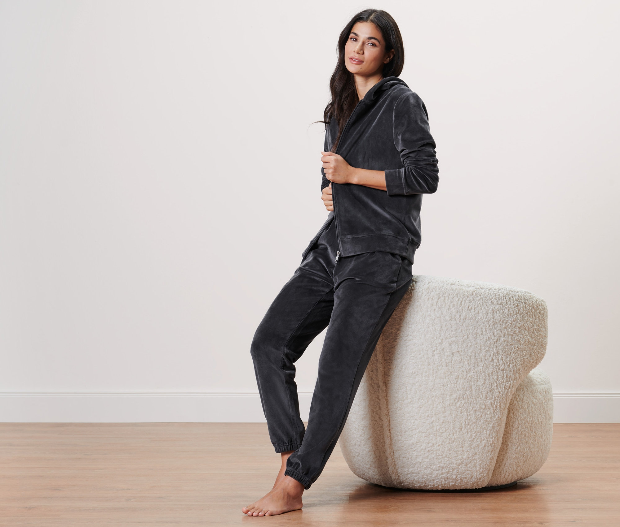 Frau sitzt in grauem Nicki-Hausanzug auf einem Hocker.