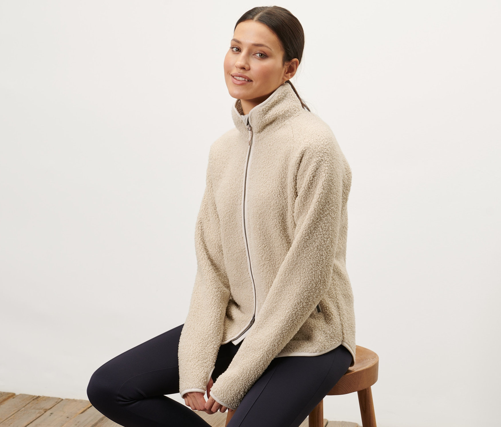 Frau sitzt auf einem Hocker und trägt eine offwhite Teddy-Jacke.