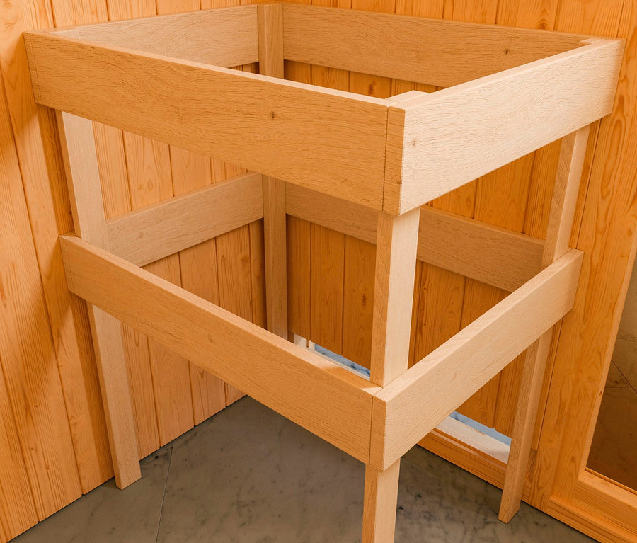 Unfertige Holzkonstruktion einer Karibu Sauna »Elli 1« steht in einem Holzzimmer auf einem grauen Boden.
