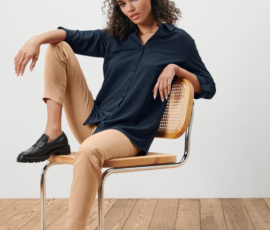 Frau sitzt auf einem Stuhl und trägt eine dunkelblaue Piqué-Jerseybluse.