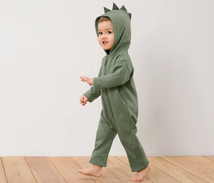Ein Kind in einem Kinder-Sweat-Overall mit Dino-Applikation geht auf einem Holzboden.