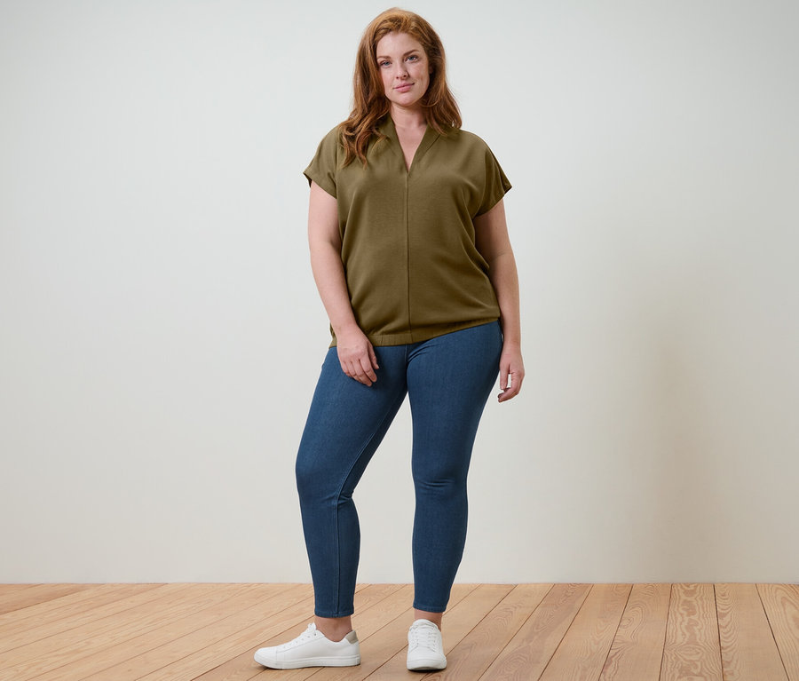 Frau posiert im Studio und trägt ein Blusenshirt mit V-Ausschnitt und Jeggings.