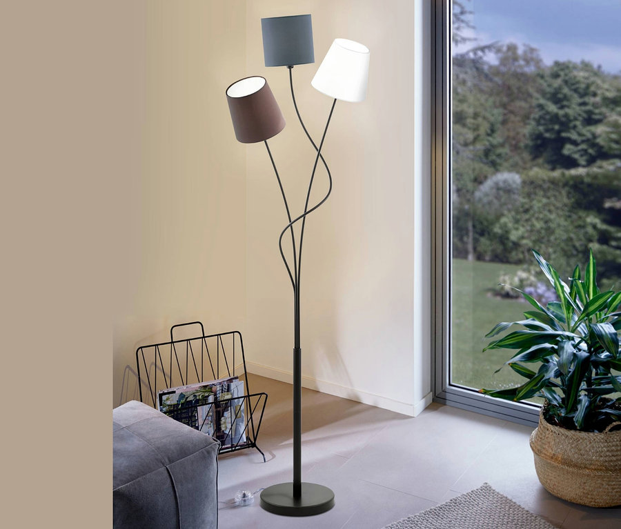 Im Wohnzimmer steht eine Eglo-Stehleuchte »Maronda« vor beigen Wänden und einem Fenster mit Blick ins Grüne.