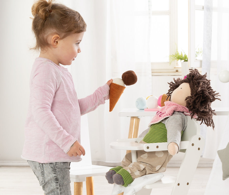 Mädchen bietet Stoffpuppe im weißen roba Puppenhochstuhl »Stella« ein Spielzeug-Eis an.