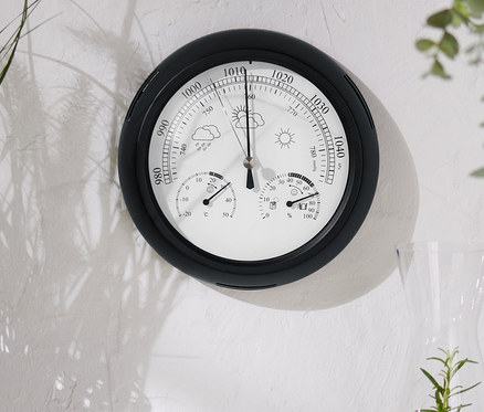 Analoge Wetterstation hängt an einer weißen Wand.