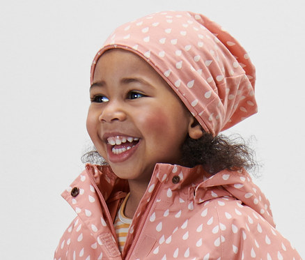 Lächelndes Mädchen trägt eine rosa Kinder-Jerseymütze und eine Regenjacke mit Kapuze.