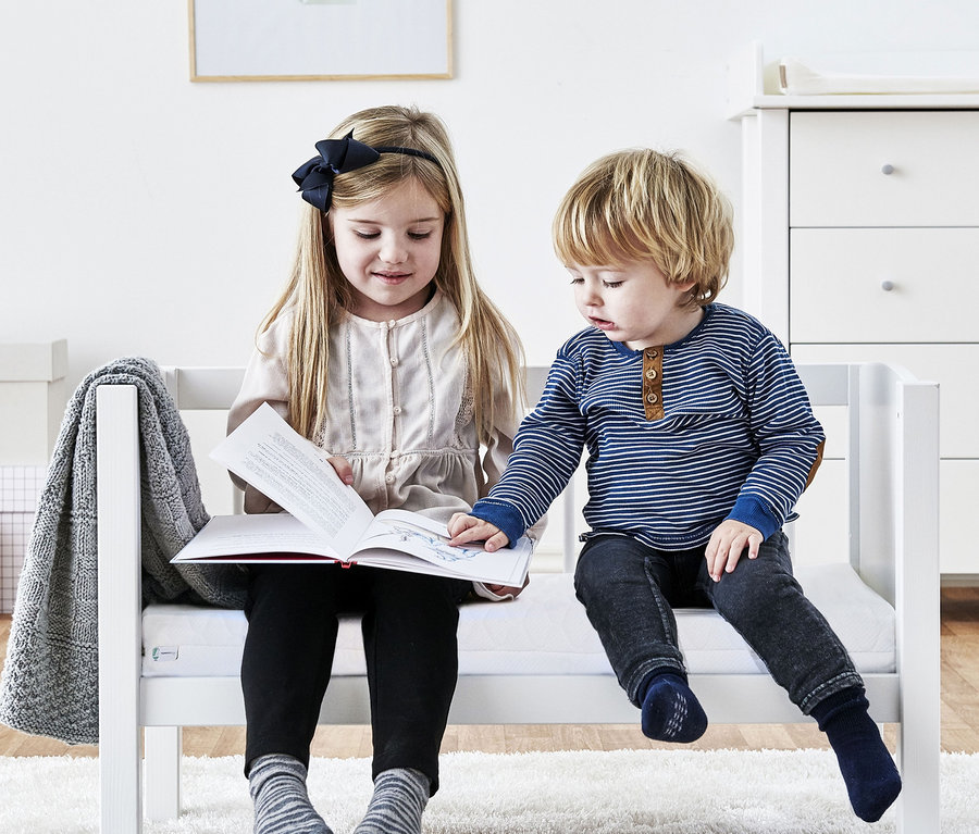 Mädchen und Junge sitzen auf Hoppekids Babywiege, ca. 40 x 80 cm, und schauen sich ein Buch an.