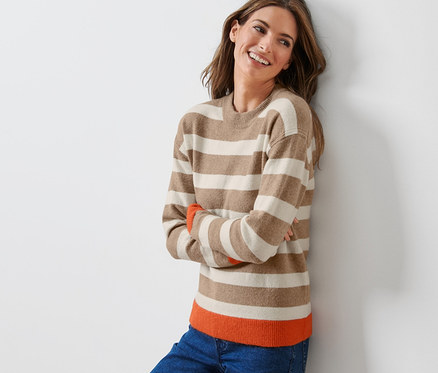 Frau lächelt an eine Wand gelehnt in einem gestreiften Strickpullover.