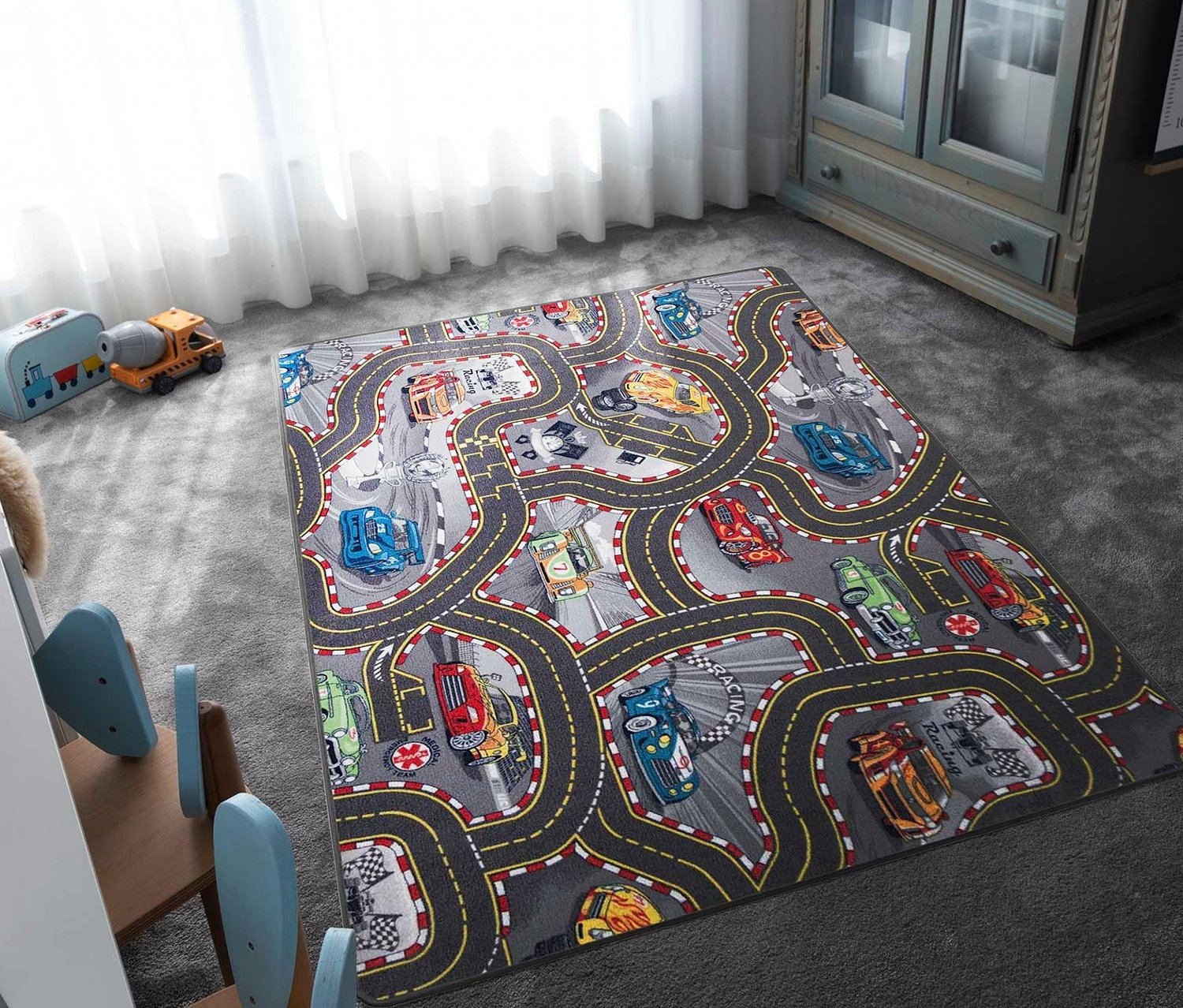 Ein Kinderteppich »CARS« mit Auto- und Rennstreckenmotiven liegt auf einem grauen Teppich im Kinderzimmer.