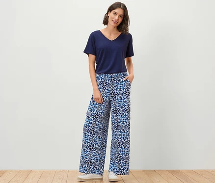 Frau steht mit Händen in den Taschen einer bedruckten Palazzohose, blau.