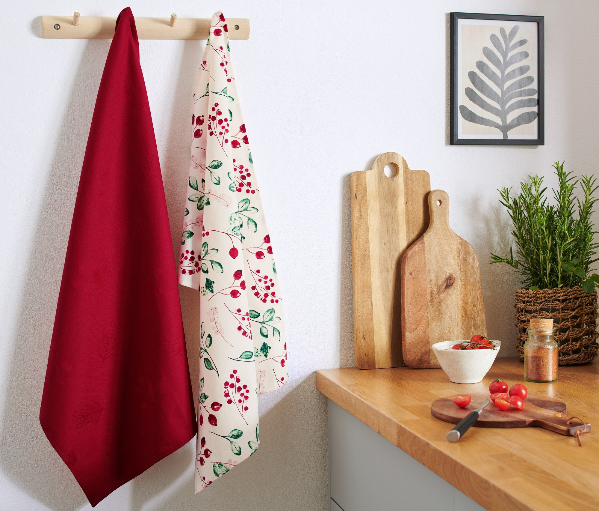 Zwei Geschirrtücher hängen an einer Stange, eines rot und eines mit Beerenmuster.