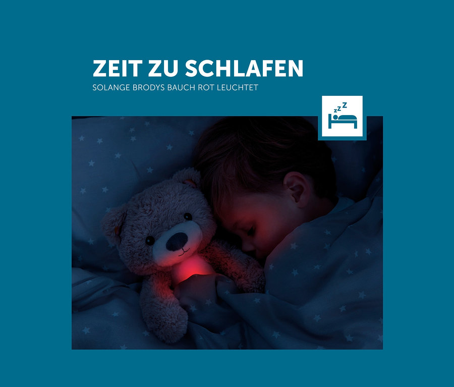 Ein Junge schläft mit dem Zazu Nachtlicht »Brody der Bär« Teddybär, dessen Bauch rot leuchtet.
