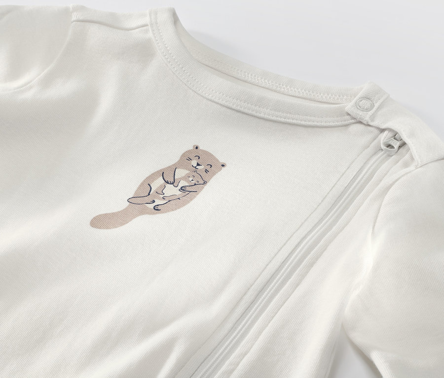 Detailansicht eines weißen Baby-Schlafanzugs mit Otter-Motiv.