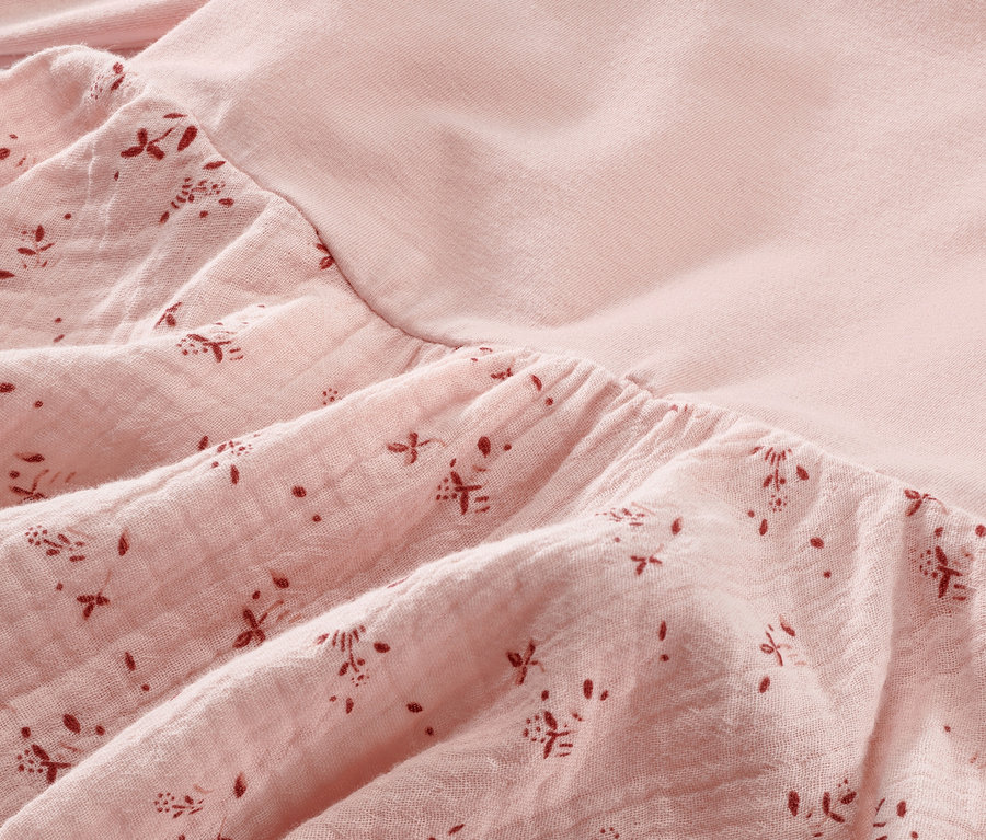 Detailansicht eines rosa Baby-Webkleids mit Blumenmuster.