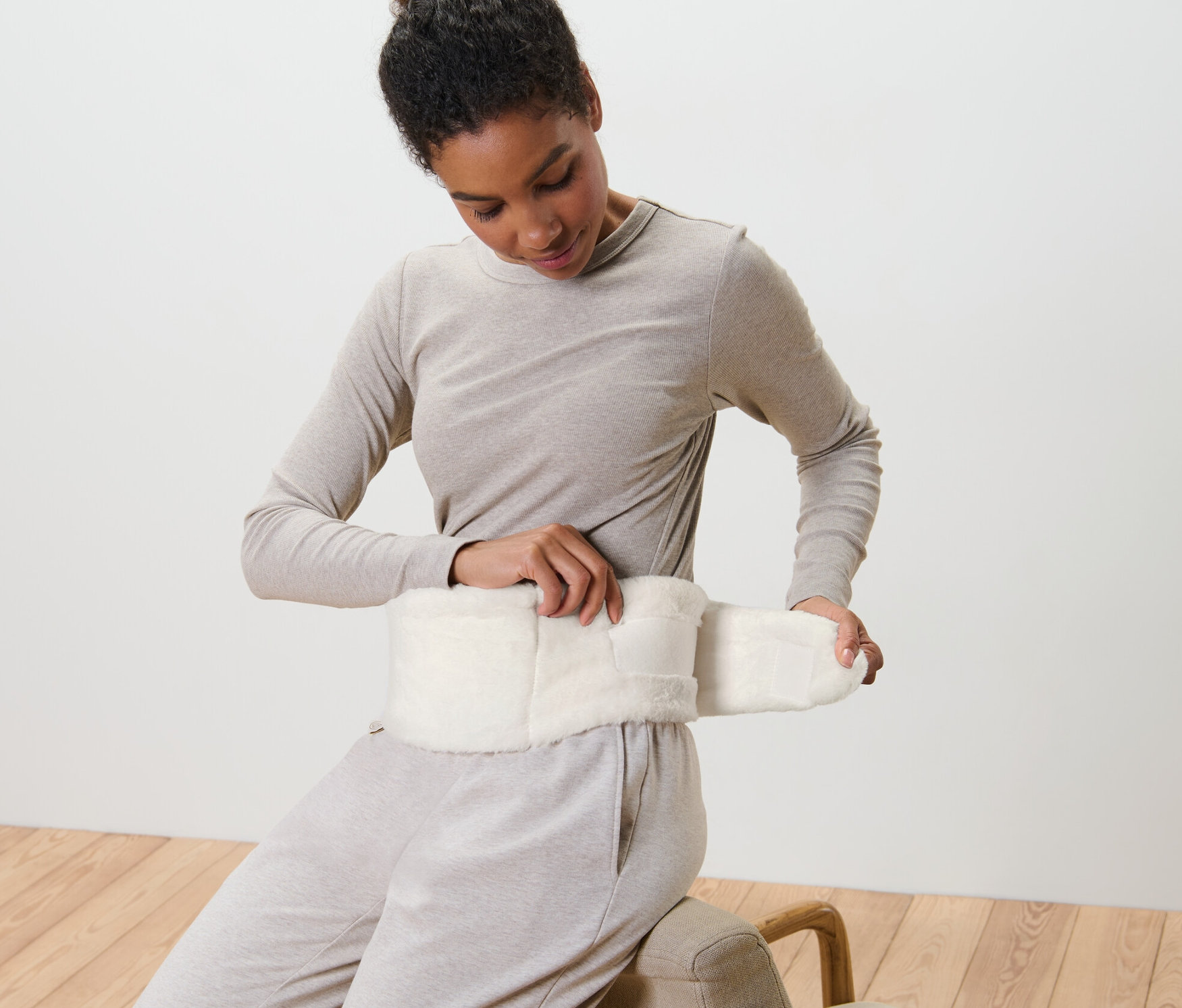 Frau befestigt eine Wärmflasche mit Band um ihre Taille.