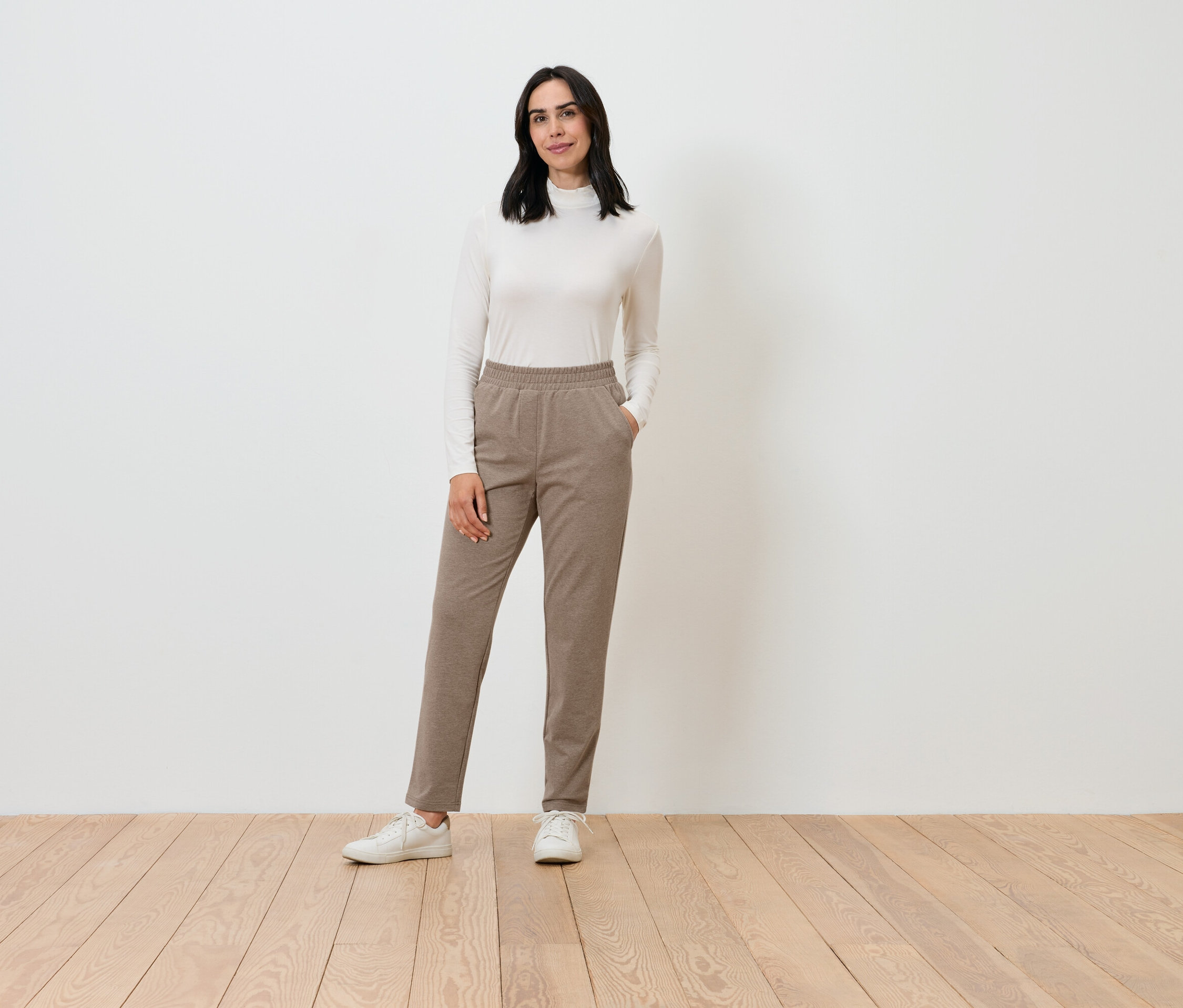 Eine Frau posiert in einem cremefarbenen Rollkragenpullover und braunen Hosen.