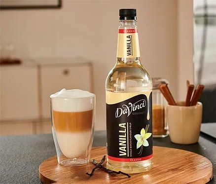 Ein Glas Getränk und eine Flasche DaVinci Vanillesirup (1 Liter) auf einem Holztablett.