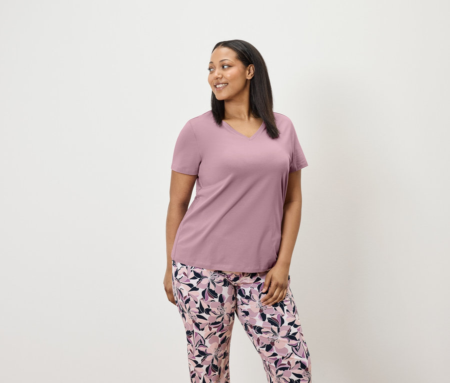 Frau in lila Kurzarm-T-Shirt und floraler Hose schaut nach rechts.