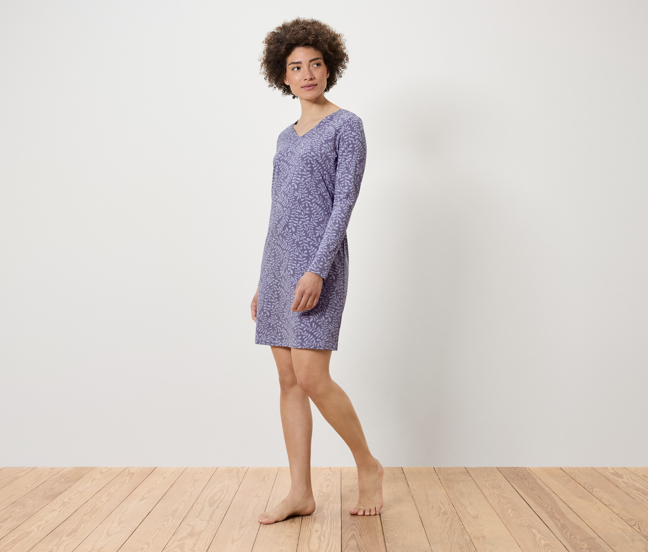 Frau posiert in einem lila, langärmeligen Kleid mit Pflanzenmuster.