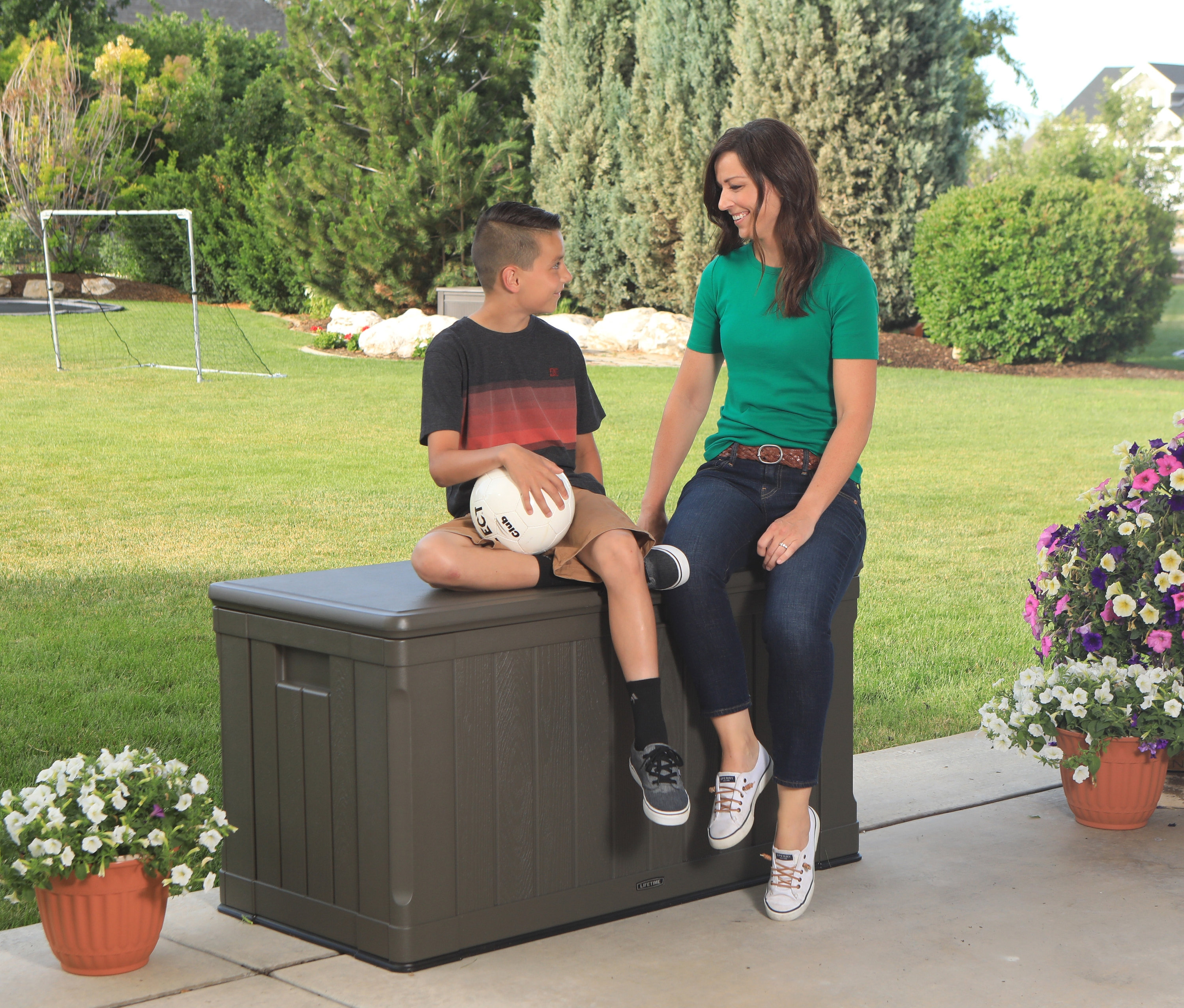 Eine Frau und ein Junge sitzen draußen auf einer braunen Lifetime-Kissenbox, ca. 440 l.