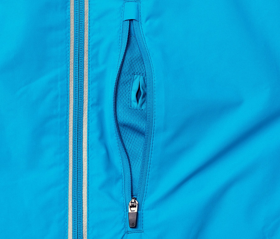 Detailansicht einer blauen Windprotection-Funktionsjacke mit teilweise geöffneter Reißverschlusstasche.