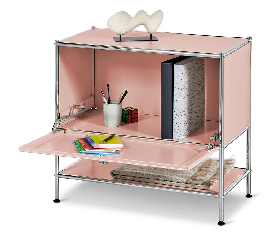 Rosa Schrank mit geöffneter Tür, innen Becher mit Stiften, Würfel und Ordner, auf dem unteren Regal eine Decke und oben eine Plastik.