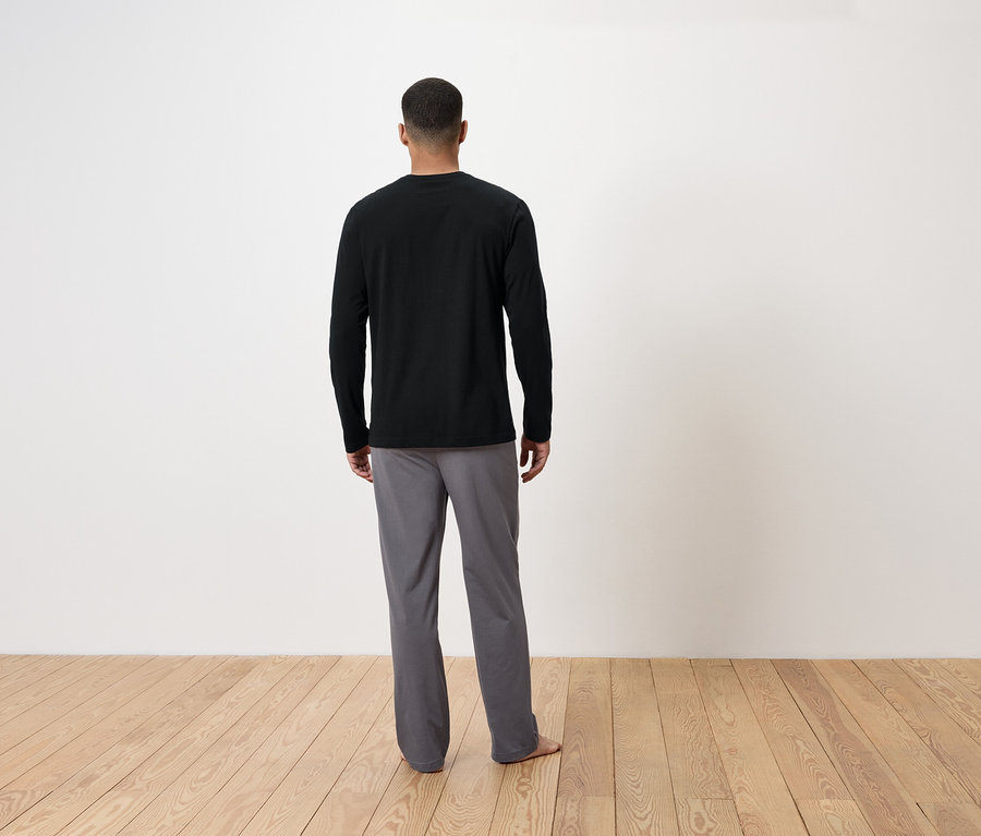 Ein Mann mit dem Rücken zur Kamera trägt ein schwarzes Langarmshirt und graue Hosen.