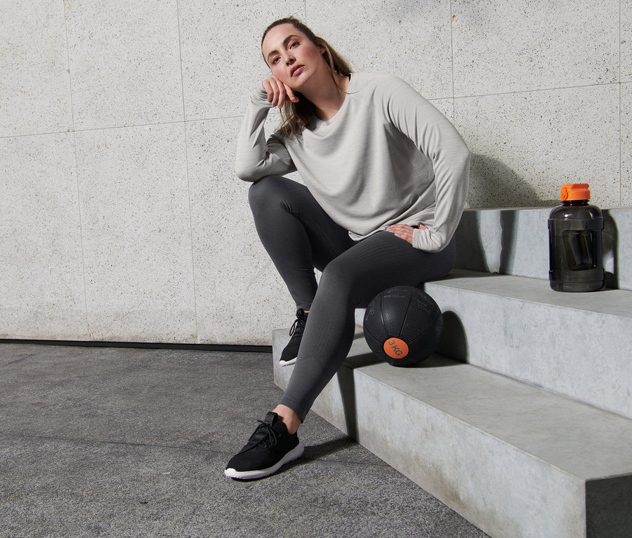 Frau sitzt auf Stufen in grauem Langarm-Funktionsshirt und Seamless-Sporttight.