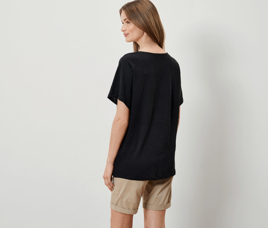 Frau posiert in schwarzem Shirt aus Leinenmix und beigen Shorts.