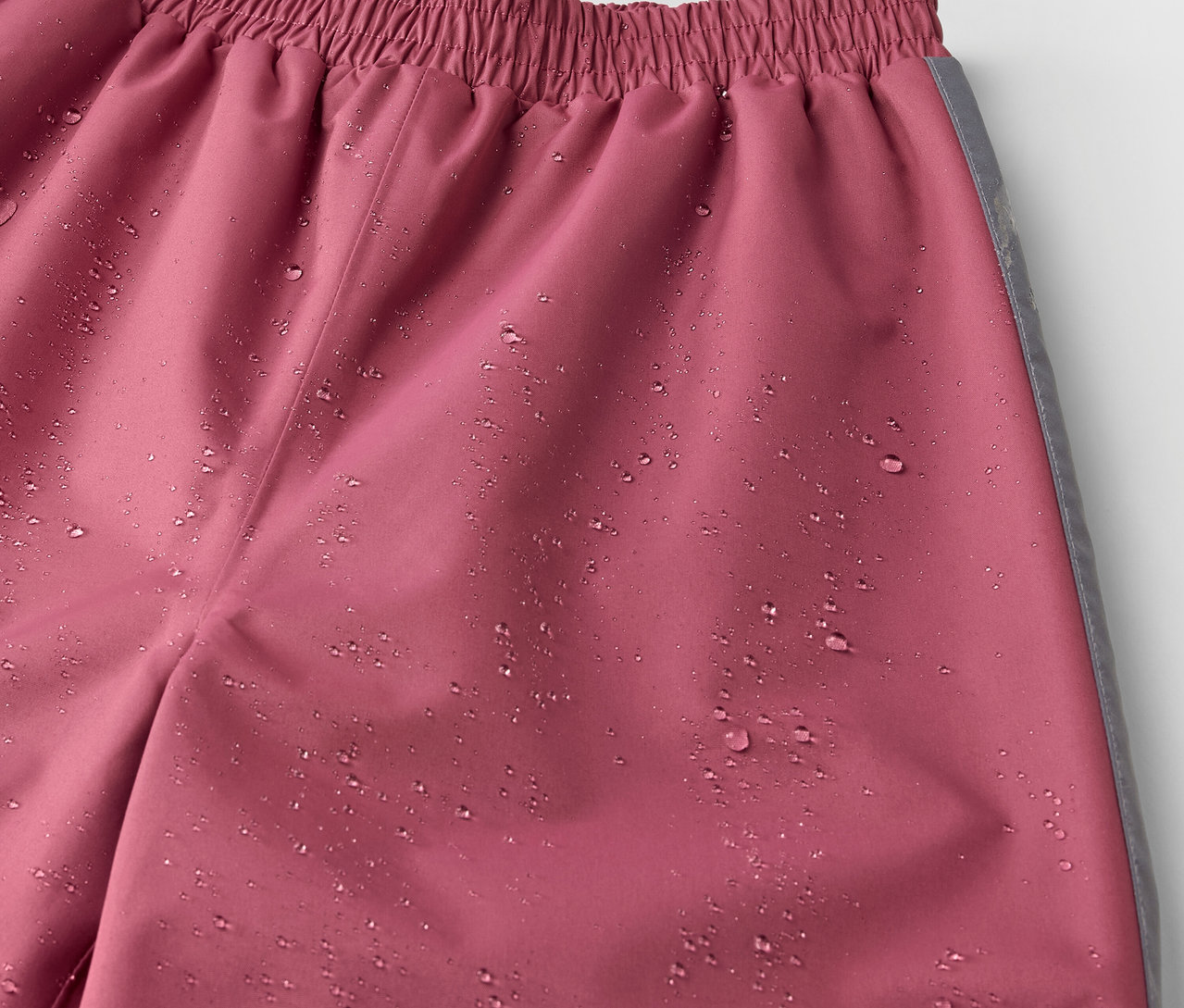Detailaufnahme einer Kinder-Regenhose in Rosa mit Wassertropfen.