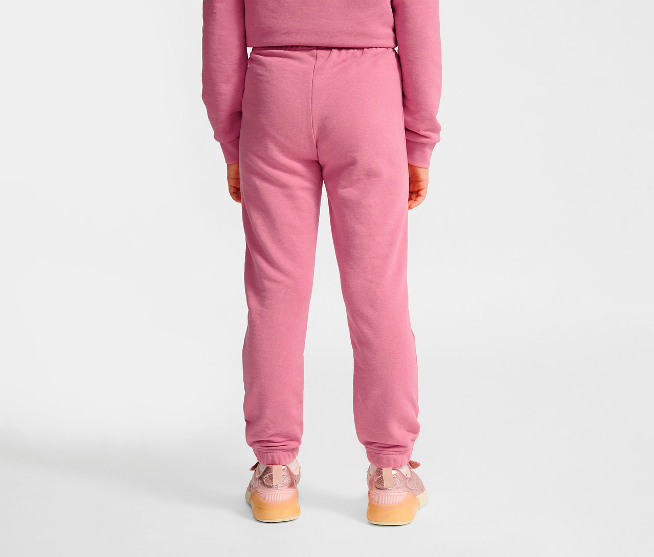 Rückansicht eines Mädchens in pinkfarbener HUMMEL HMLJR Base Regular Pants und Turnschuhen.