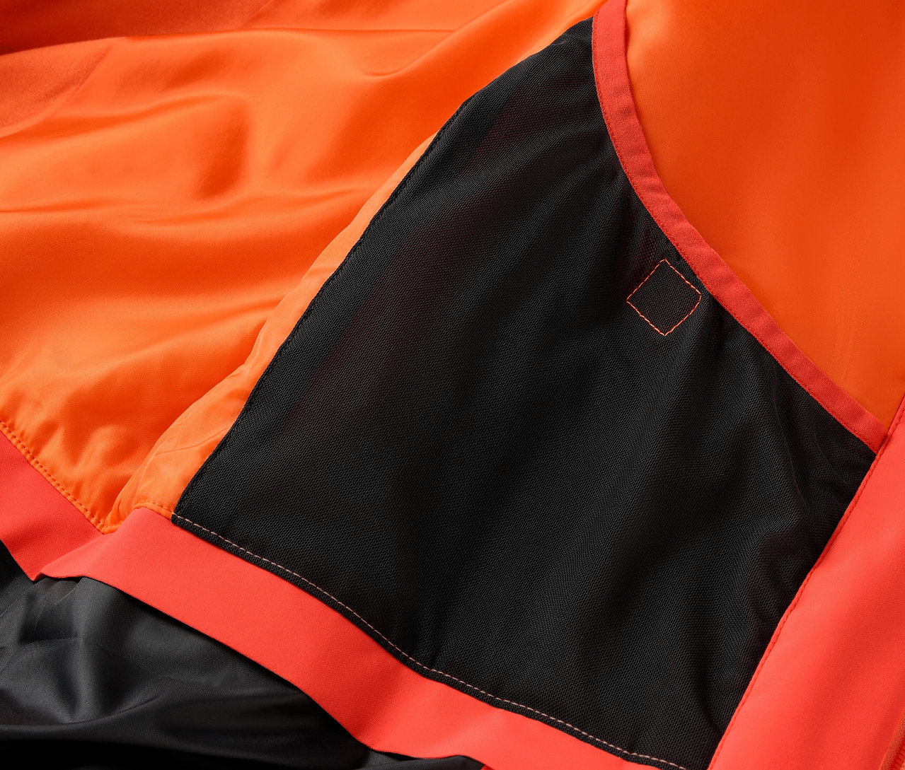 Detail einer orangefarbenen Jacke mit schwarzer Tasche.