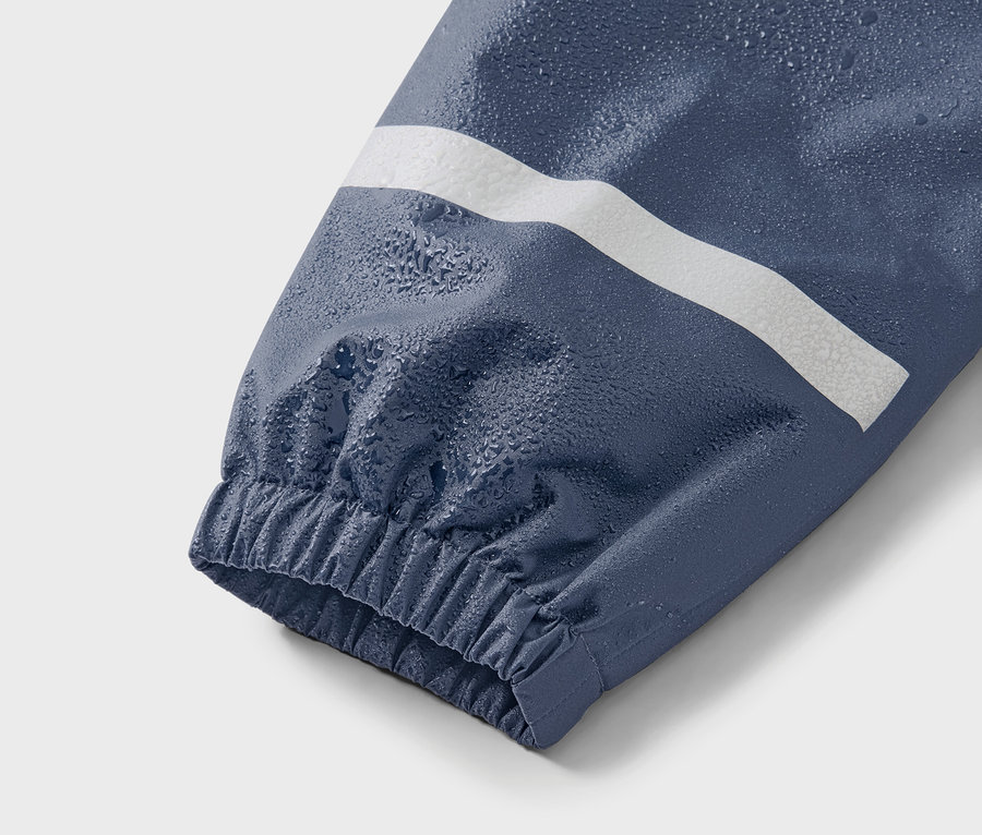 Nahaufnahme eines blauen Jackenärmels mit einem weißen Streifen und Wassertropfen.