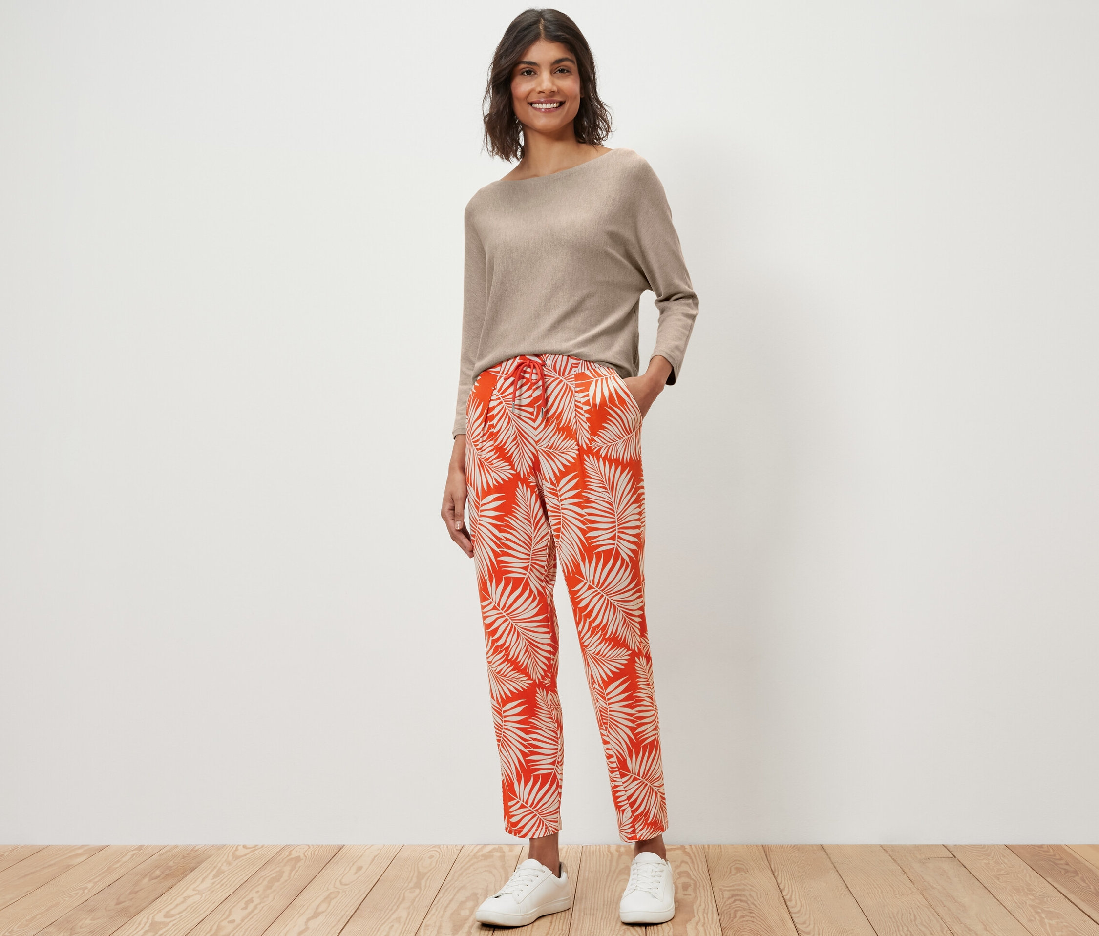 Frau steht in einem beige Oberteil und einer bedruckten Jerseyhose.