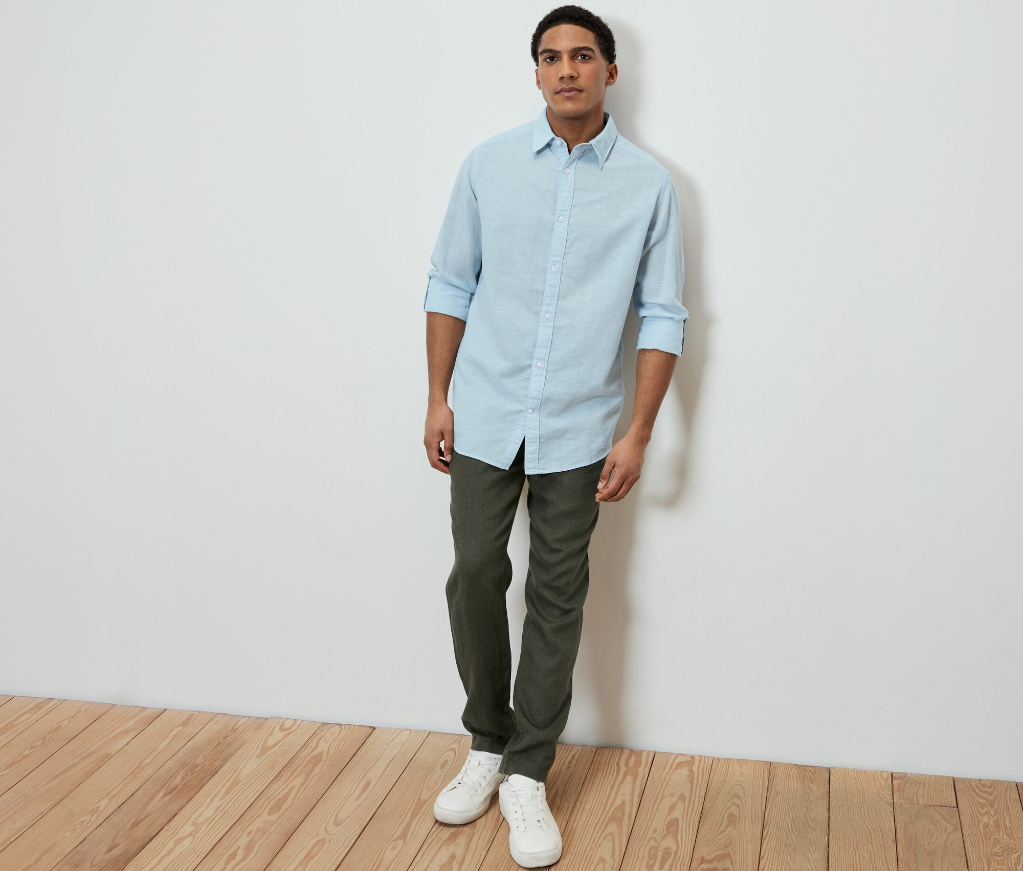 Mann trägt ein hellblaues Hemd mit Leinen, grüne Hose und weiße Sneaker.