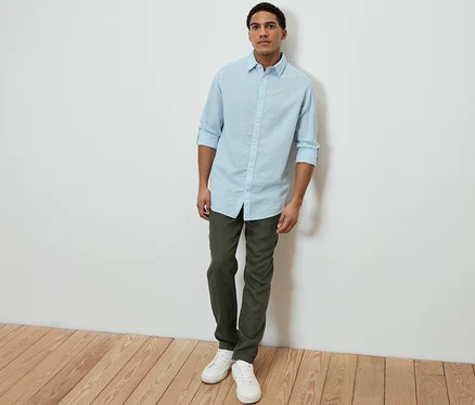 Mann trägt ein hellblaues Hemd mit Leinen, grüne Hose und weiße Sneaker.