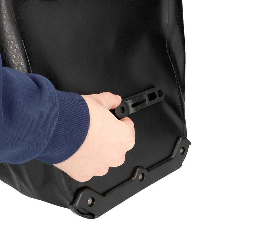 Eine Hand befestigt eine schwarze Halterung an einer schwarzen Tasche.